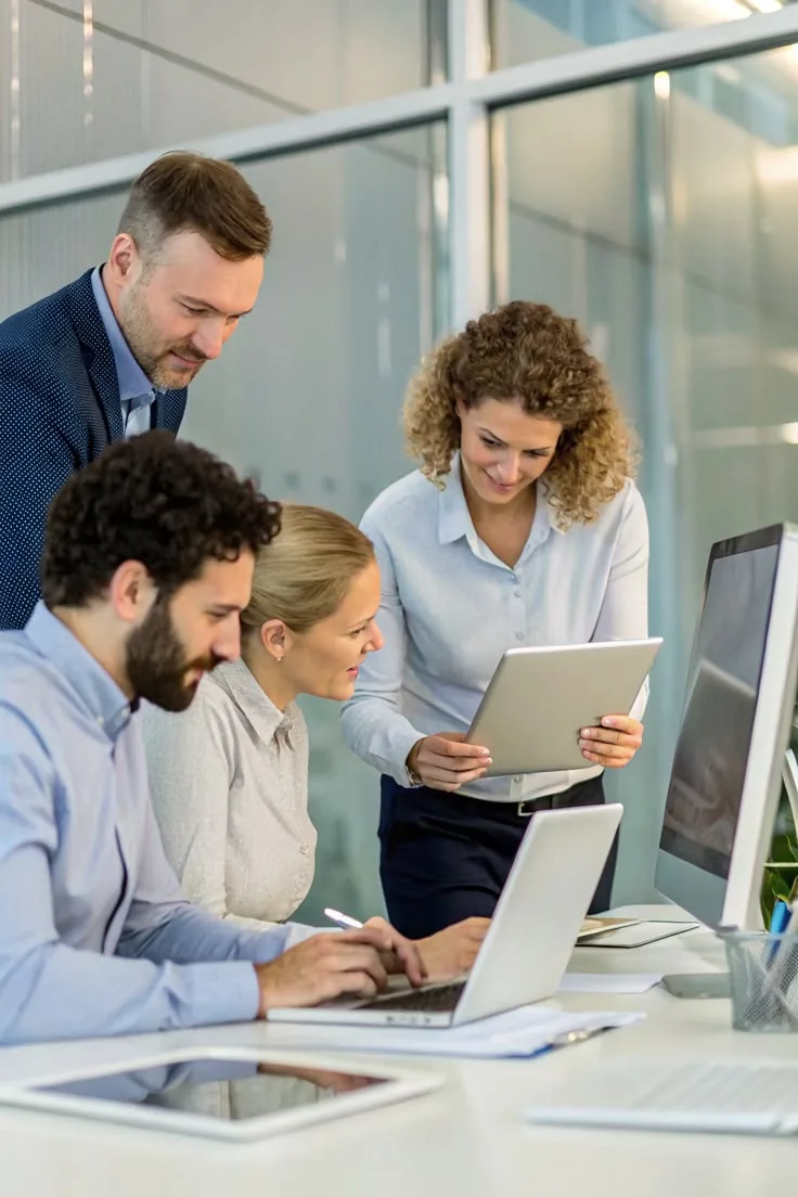 Four colleagues reviewing work together around a laptop